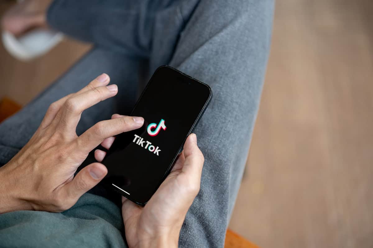 Close-up de uma mão de homem segurando smartphone abrindo aplicativo TikTok.