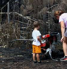 Uma mãe e seu filho inspecionam os arredores de sua casa em Le Porge, na segunda-feira, após ela ter sido destruída por um incêndio florestal Foto: Reuters / BBC News Brasil
