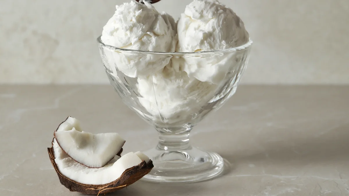 Foto colorida de sorvete de coco em taça com fruta ao lado