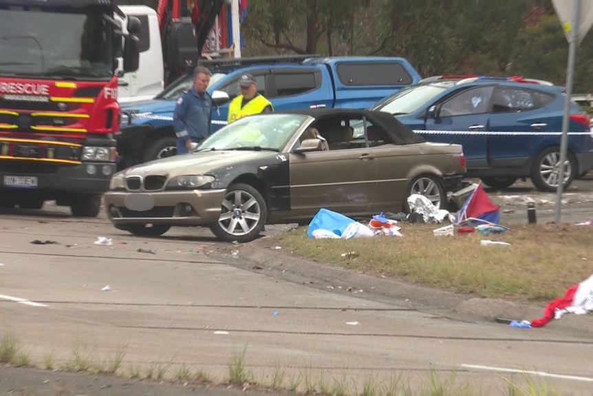 Brown car stationary, fire truck and emergency officers standing behind it.
