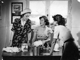 Black and white photo from 1940s or 1950s showing three women making a cake in a rural kitchen